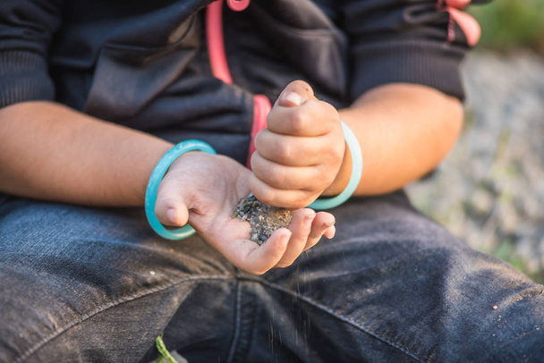 Vista cercana de las manos de niña mientras juega en el suelo con alma o piedras pequeñas
. - Foto, Imagen