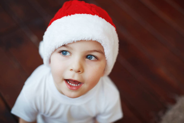 Niño en sombreros de Navidad está sentado con cajas de regalo en sus manos con la alegría de una sorpresa
. - Foto, Imagen