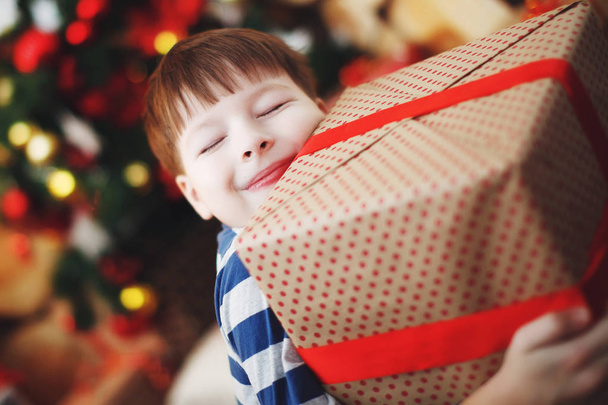 Хлопчик у різдвяних капелюхах сидить з подарунковими коробками в руках з радістю від несподіванки
. - Фото, зображення