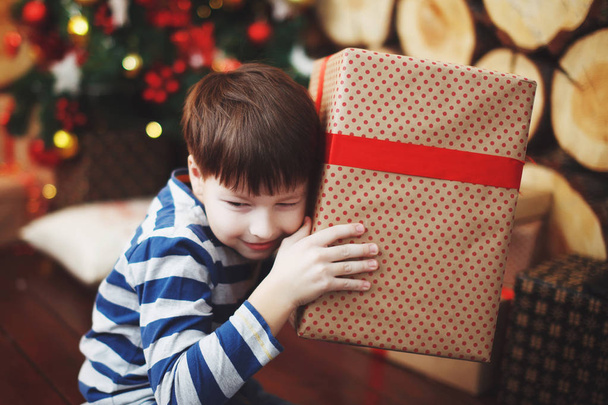 Menino de chapéus de Natal está sentado com caixas de presente em suas mãos com a alegria de uma surpresa
. - Foto, Imagem