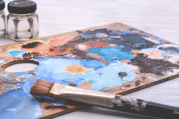 Artist's palette with colorful oil paint strokes and paintbrushes on white wooden background. Art concept - Фото, зображення