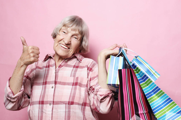 glückliche Großmutter mit Einkaufstaschen vor rosa Hintergrund. Lebensstil und Menschen-Konzept. - Foto, Bild