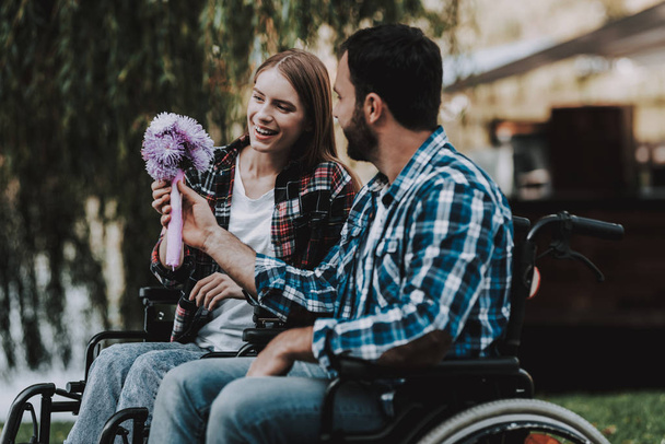 Couple of Disabled People on Wheelchairs on Date in Park. Young Man with Flowers. Woman on Wheelchair. Date in Summer Park. Romantic Relationship. Recovery and Healthcare Concepts. Happy Couple. - Photo, Image