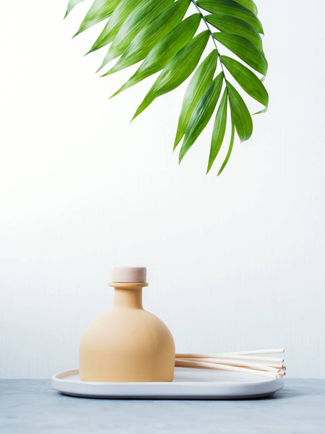 aroma reed fragrance diffuser with rattan sticks and green palm leaf on light grey background - Foto, Imagen
