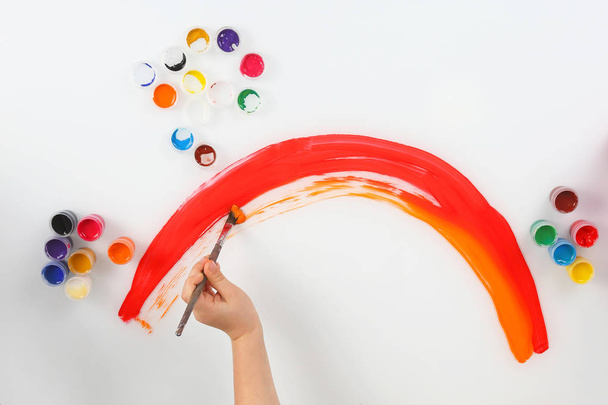 mão da criança desenha um arco-íris em um fundo branco
 - Foto, Imagem
