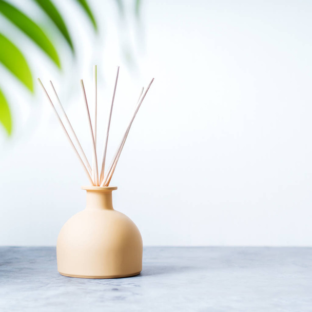 aroma reed fragrance diffuser with rattan sticks and green palm leaf on light grey background - Фото, зображення