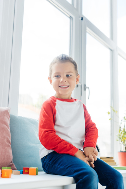 portrait of cute cheerful boy sitting at window at home - Foto, Bild