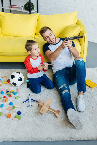 улыбающийся мужчина и симпатичный сын играют с игрушками вместе на полу дома
 - Фото, изображение