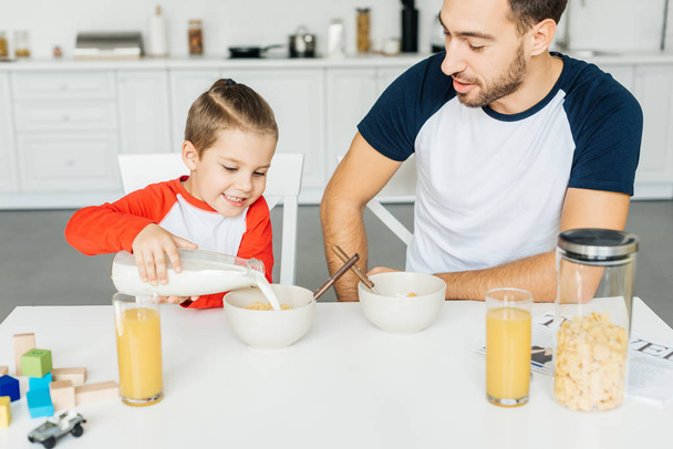 happy father and little son having breakfast together in kitchen at home - Фото, изображение