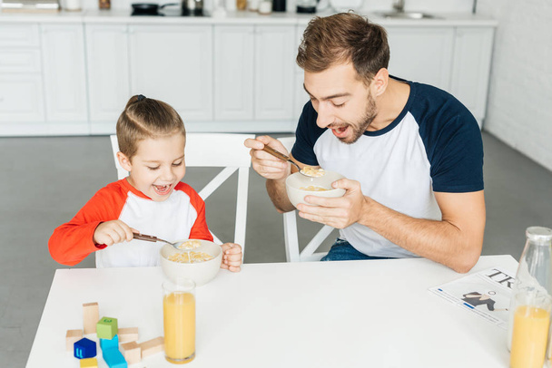happy father and little son having breakfast together in kitchen at home - Фото, зображення