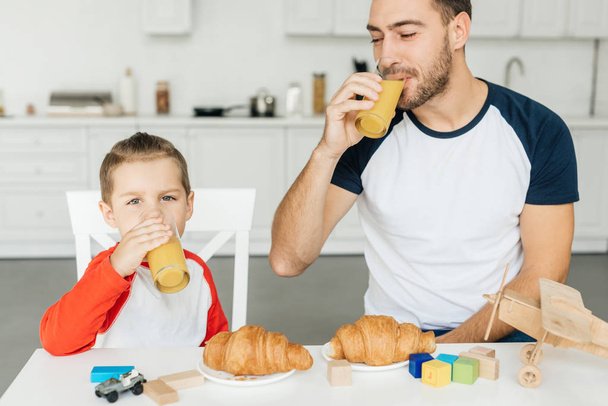 young father and son having breakfast with croissants and orange juice together at home - Foto, afbeelding