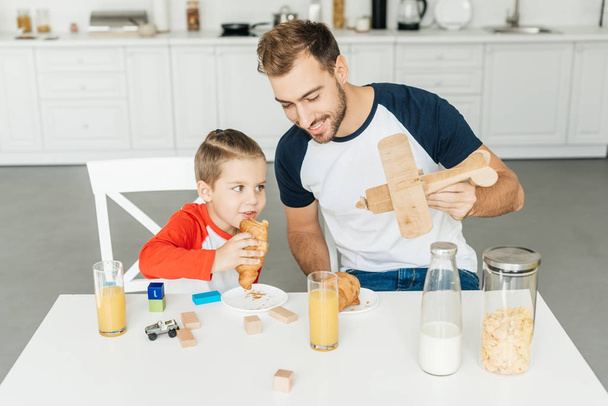 przystojny młody ojciec i syn, grając z samolotu zabawka jedząc śniadanie razem w domu - Zdjęcie, obraz