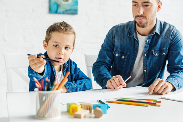 handsome young father drawing with adorable little son at home - Фото, изображение