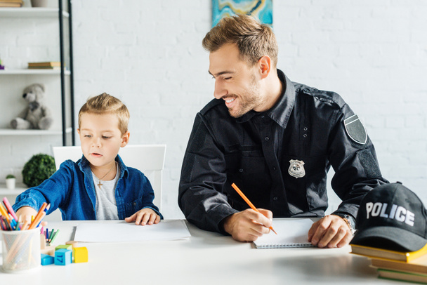 Polis üniforması ve küçük oğlu evde çizim birlikte mutlu genç baba - Fotoğraf, Görsel