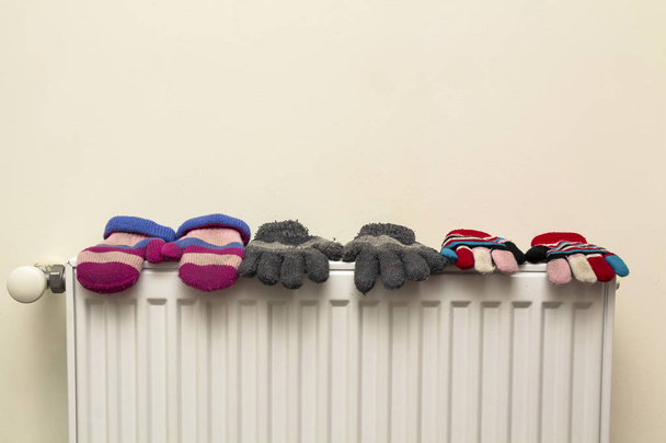 Luvas de lã listradas de malha de mão quente das crianças que secam no radiador de aquecimento após o dia de inverno fora
 - Foto, Imagem
