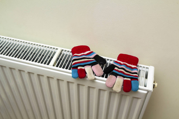 Guantes de lana rayados de punto a mano calientes de los niños que se secan en el radiador de calefacción después del día de invierno afuera
 - Foto, Imagen