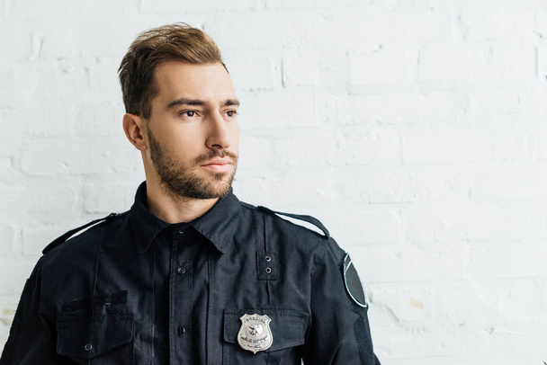 portrait of thoughtful young policeman in front of white brick wall - Photo, Image