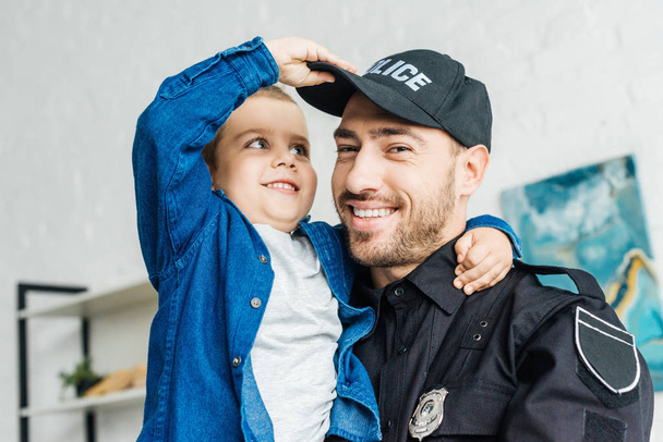 close-up portrait of smiling young father in police uniform carrying his little son and looking at camera - Fotografie, Obrázek