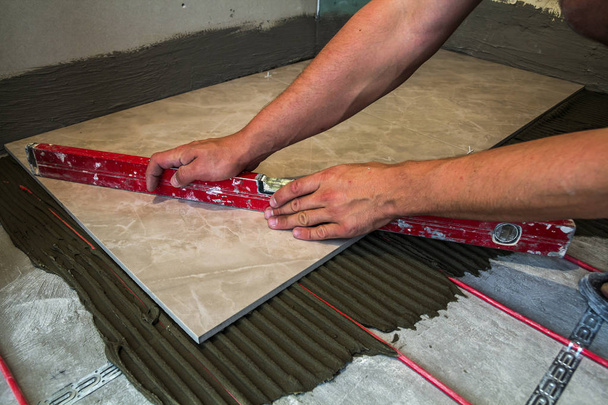 Keramische tegels en hulpmiddelen voor de tegelzetter. Werknemer hand vloertegels installeren. Verbetering van het huis, renovatie - keramische tegel vloer lijm, mortel, niveau. - Foto, afbeelding