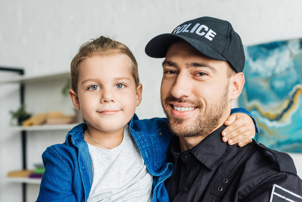 happy young father in police uniform carrying his little son and looking at camera - Fotoğraf, Görsel