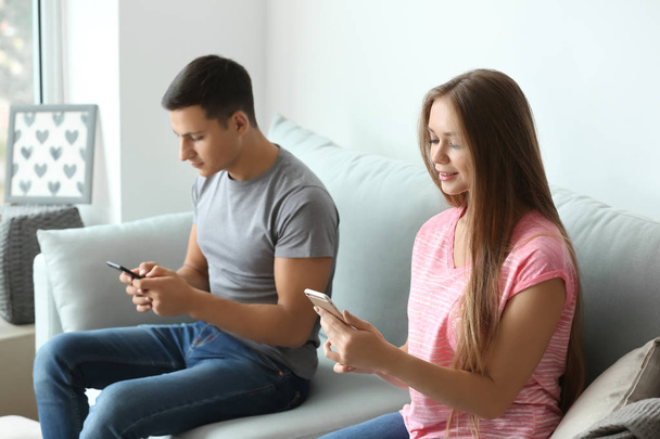 Cep telefonlarıyla evde koltukta oturan genç çift - Fotoğraf, Görsel