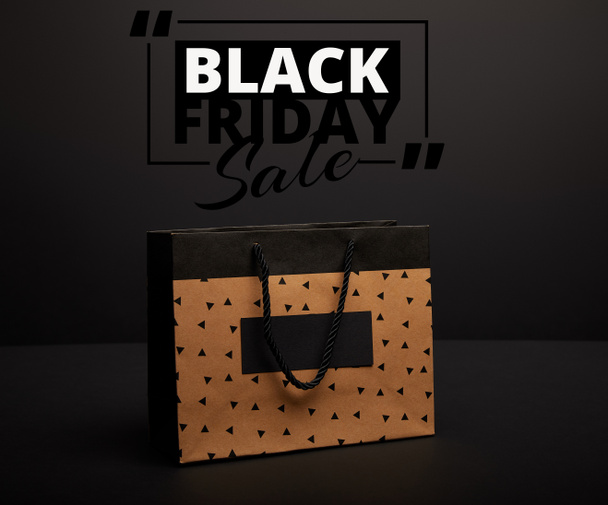 close up view of paper shopping bag on black with black friday sale - Foto, Bild