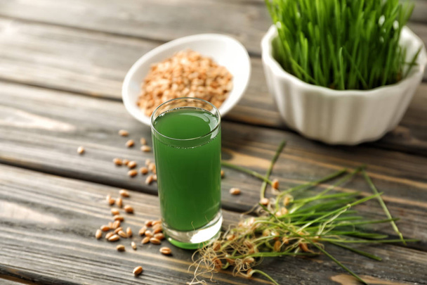 Glass of fresh wheat grass juice on wooden table - 写真・画像
