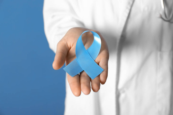 Female doctor holding blue ribbon on color background, closeup. Cancer awareness concept - Zdjęcie, obraz