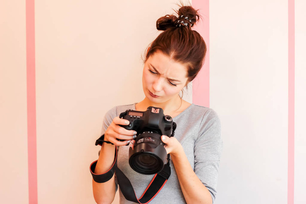 Όμορφο κορίτσι φωτογράφος εξετάζει τη φωτογραφική της μηχανή και κάνει αστείο δυσαρεστημένοι πρόσωπο - Φωτογραφία, εικόνα
