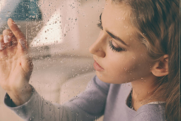 Mulher solitária deprimida perto da janela em casa, vista através do vidro
 - Foto, Imagem