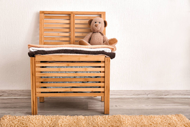 Wooden laundry box with towels and toy bear on floor near white wall - Foto, Imagen
