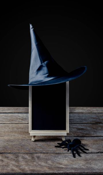 Halloween achtergrond. schoolbord op de tribune, heks hoed met zwarte spin op de houten vloer en een zwarte achtergrond - Foto, afbeelding