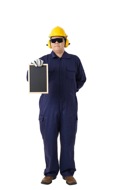 Volledige lichaam portret van een werknemer in Mechanic Jumpsuit met helm oorkappen, beschermende handschoenen en veiligheid bril bedrijf schoolbord geïsoleerd op een witte achtergrond uitknippad - Foto, afbeelding