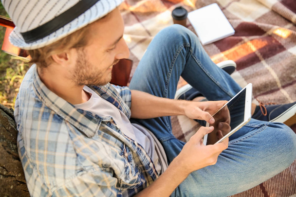 Handsome young man with tablet PC resting on plaid in park - Photo, Image