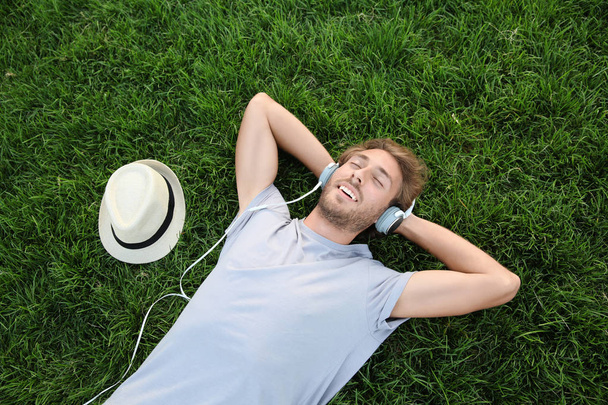 Όμορφος νεαρός άνδρας, να ακούτε μουσική στο πράσινο γρασίδι στο πάρκο - Φωτογραφία, εικόνα
