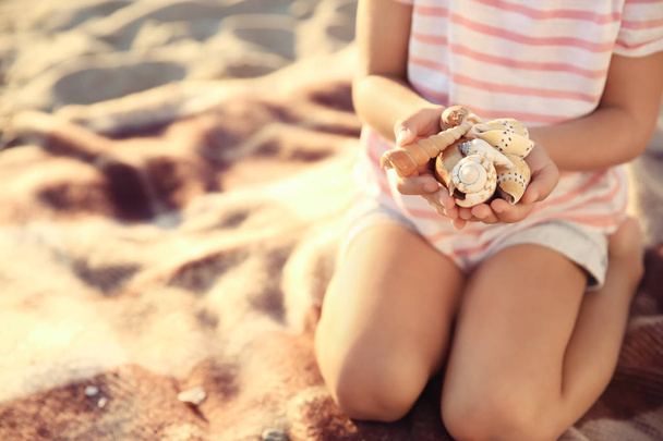 Nettes kleines Mädchen mit Muscheln am Strand - Foto, Bild