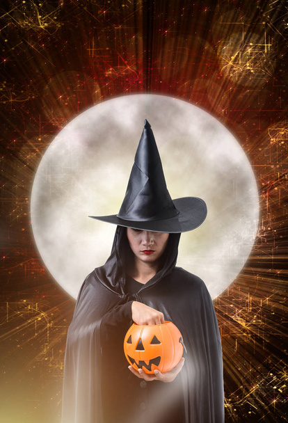 Portret van een vrouw in zwarte Schrikachtig heks halloween kostuum bedrijf halloween pompoen, magische verlichting en grote maan met Halloween kunst ontwerp achtergrond - Foto, afbeelding