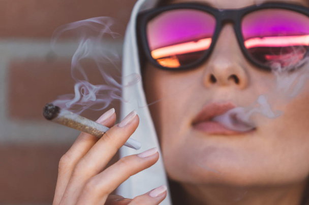 Portrait of a girl smoking marijuana joint on the street of Amsterdam (Holland - Netherlands) - medical marijuana use and legalization of cannabis, pregnant woman dangerous smoking concept - Zdjęcie, obraz