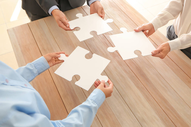 Business team holding pieces of puzzle over wooden table, closeup - Photo, Image
