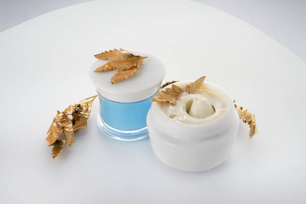 Pots avec crème pour le corps et feuilles dorées sur fond blanc
 - Photo, image