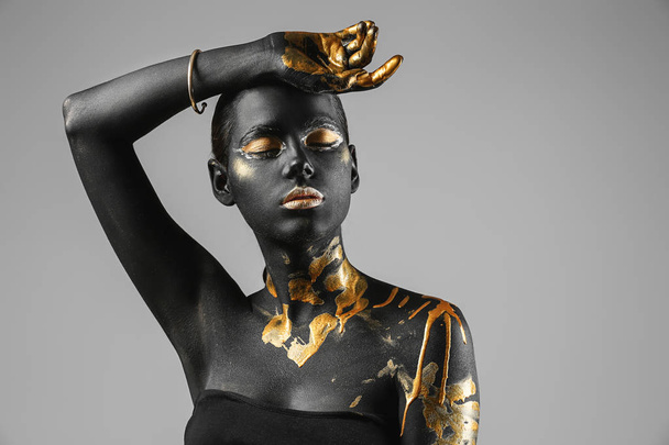 Beautiful woman with black and golden paint on her body against light background - Photo, Image