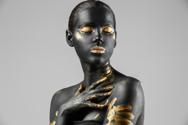 Όμορφη γυναίκα με το μαύρο και το χρυσό χρώμα στο σώμα της ενάντια σε ανοιχτόχρωμο φόντο - Φωτογραφία, εικόνα