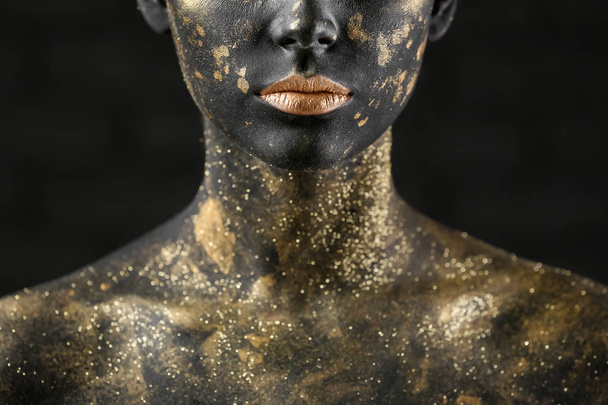 Mulher bonita com tinta preta e dourada em seu corpo contra fundo escuro, close-up
 - Foto, Imagem