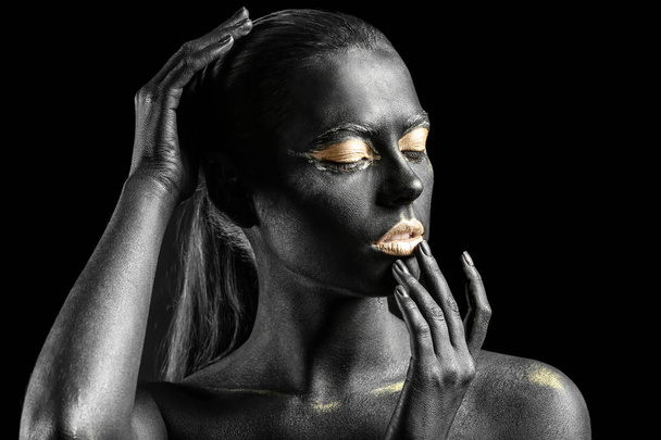Beautiful woman with black and golden paint on her body against dark background - Valokuva, kuva