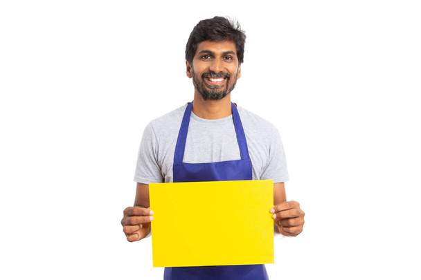 freundliche indische Geschäft oder Supermarkt Mitarbeiter halten gelbes Papier mit leeren Kopie Textbereich isoliert auf weißem Hintergrund - Foto, Bild