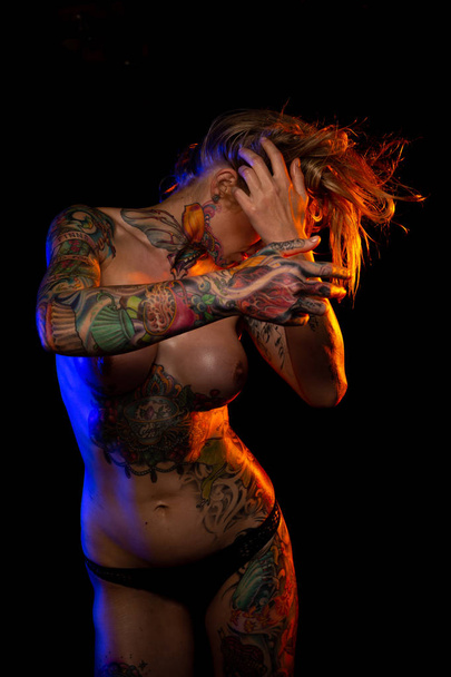 Muscled caucasian woman with tattoos and oiled skin poses under colored lights - Foto, Imagem