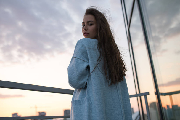 Attractive young woman stands against city and sunset. - 写真・画像