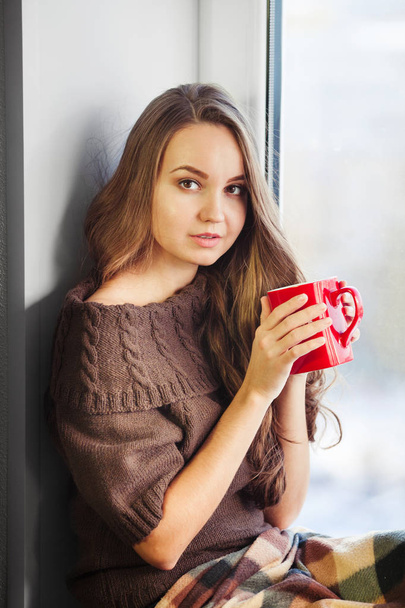 Woman sitting on window sill and drinking cup of coffee - Zdjęcie, obraz