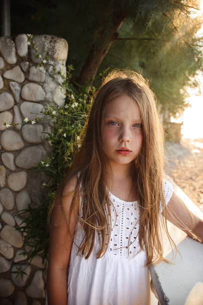 beautiful little girl in white dress standing near stone wall outdoor  - Fotografie, Obrázek
