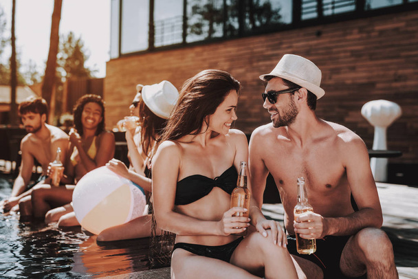 Smiling Couple with Alcoholic Drinks at Poolside. Beautiful Young Couple holding Bottles of Beer and having Fun at Poolside. Happy Friends Enoying Pool Party. Summer Vacation Concept - Photo, Image